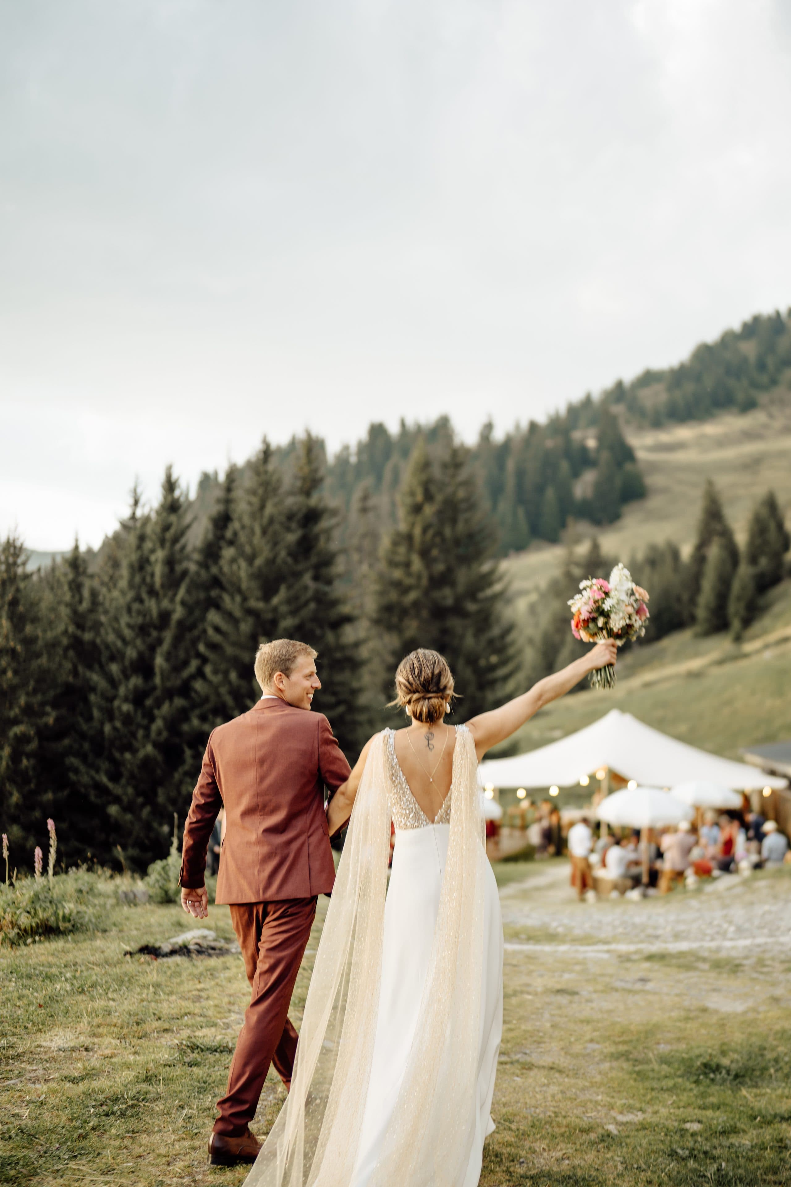 Mariés marchant vers la fête en alpage, bouquet levé, Valais